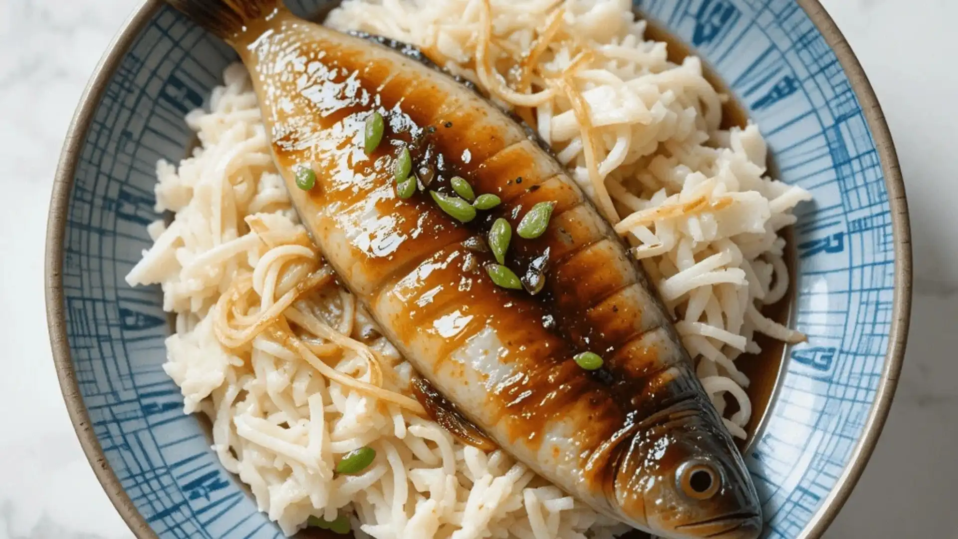 Steamed fish served with rice, drizzled with soy sauce and garnished with green seeds.