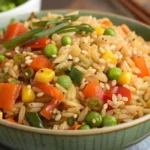 A bowl of vegetable fried rice with peas, corn, carrots, and red bell peppers, garnished with fresh green onions.