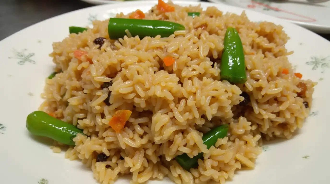 A plate of vegetable fried rice with green chilies, carrots, and raisins, served on a white dish with a floral design.