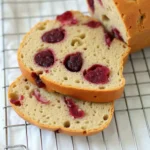 Slices of homemade raspberry sourdough bread with a golden crust and soft, airy interior, featuring whole raspberries baked into the dough, resting on a cooling rack.