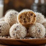 A close-up of delicious no-bake Moose Farts dessert balls coated in shredded coconut, with one cut open to reveal a soft, chewy center filled with chocolate chips.