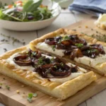 Goat cheese tart with caramelized onions and herbs on puff pastry, served on a wooden board.